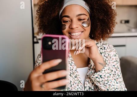 Junge, wunderschöne, lächelnde afrikanerin mit Augenklappen, die zu Hause Selfie macht Stockfoto