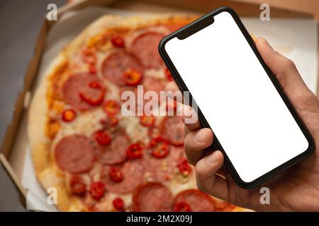 Männliche Hand mit Telefon und Pizza im Hintergrund Stockfoto