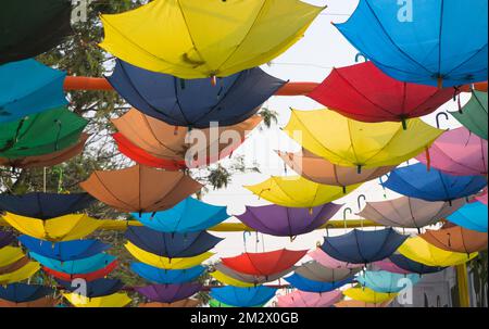 Mehrfarbige Regenbogenschirme, die auf dem Kopf hängen, als Straßenkunst. Farbenfrohe Ansicht. Stockfoto