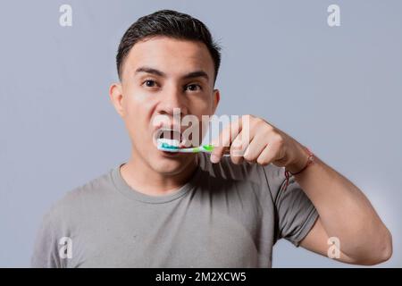 Ein gutaussehender Typ putzt sich die Zähne isoliert, Nahaufnahme eines gutaussehenden Mannes, der sich die Zähne putzt. Bürsten und zahnhygienisches Konzept. Nahaufnahme von Menschen Stockfoto