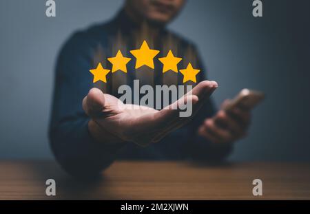 Hand eines Kunden oder Kunden, der die Sterne hält, um fünf Sterne zu vervollständigen. Mit Kopierbereich. Mit fünf Sternen bewertet. Servicebewertung, Zufriedenheitskonzept. Stockfoto