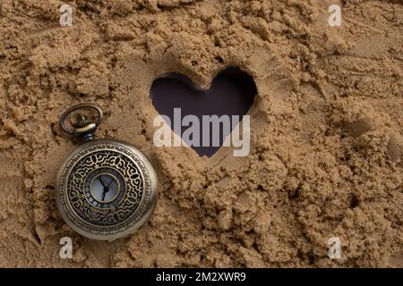 Retro Style Watch neben eine Herzform auf Sand Stockfoto