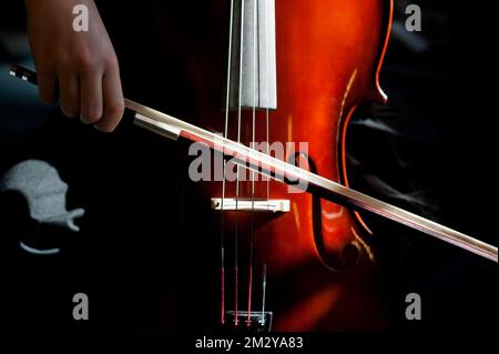 Nahaufnahme des Cello, das mit der Hand gespielt wird und sich im Schuss mit Sonnenlicht und Schatten verbeugt Stockfoto