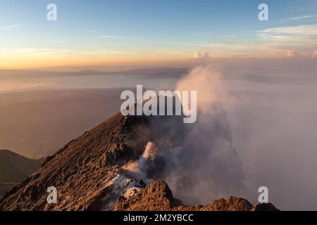 Am Rand des Merapi-Vulkankraters klettern Menschen bei Sonnenaufgang den Gipfel hinauf. Rauchende Caldera in Java, Indonesien. Stockfoto