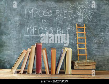 Ein Stapel Bücher mit dem Slogan Impossible ist an der Tafel unmöglich. Lernen, Bildung, Entwicklung, Leiter des Erfolgs und zurück-zur-Schule-Konzept Stockfoto