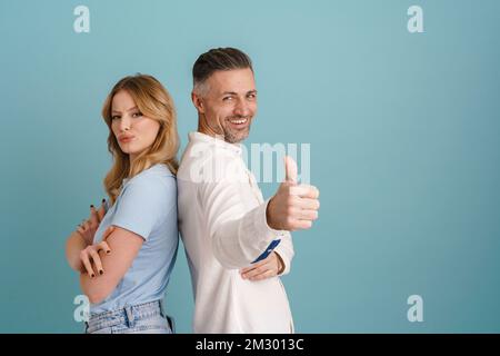 White happy man and upset woman standing back to back with different emotions isolated over blue background Stock Photo