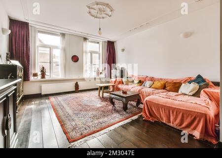 a living room with an orange couch and colorful rugs on the hardwood floor in front of the sofa is a wood burning stove Stock Photo