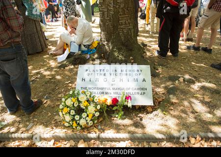 Die Menschen versammeln sich in der Nähe des Kirschbaums, der zum Gedenken an die Opfer von Hiroshima während einer Gedenkveranstaltung am Tavistock Square im Zentrum von London gepflanzt wurde. Stockfoto