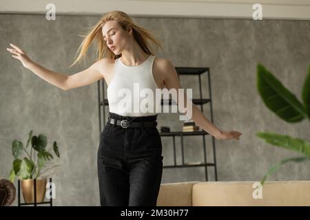 Blonde Frau mit ausgestreckten Händen, die beim Tanzen zu Hause Lippen schmollt, Stock Image Stockfoto