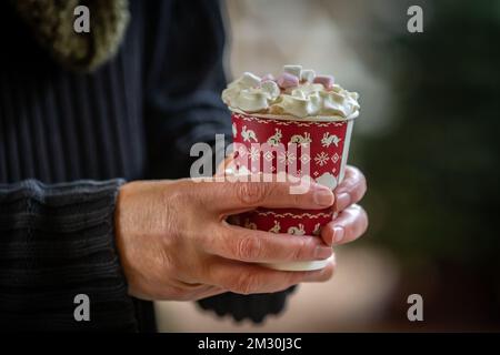 Nahaufnahme eines männerhändes mit einem heißen Schokoladengetränk, dekoriert mit Sahne und Marshmallows Stockfoto