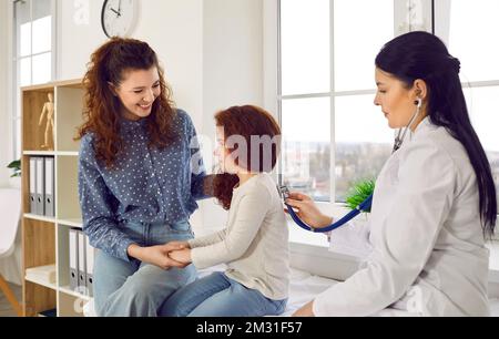 Fröhliche Frau mit Tochter besucht Kinderarzt und hält Kinderhand sitzt im Krankenhaus Stockfoto