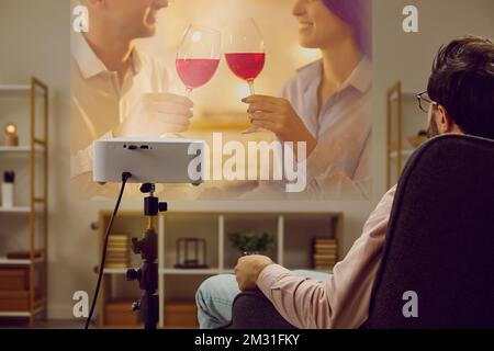 Einsamer Mann entspannt sich zu Hause am Abend und sieht sich romantische Filme auf dem Fernsehprojektor an. Stockfoto