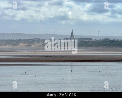 Häuser, Dünen und der Kirchturm von Coatham Church vor den Cleveland Hills und ein bedeckter Himmel von der reflektierenden Niedrigwasserküste des Strandes. Stockfoto