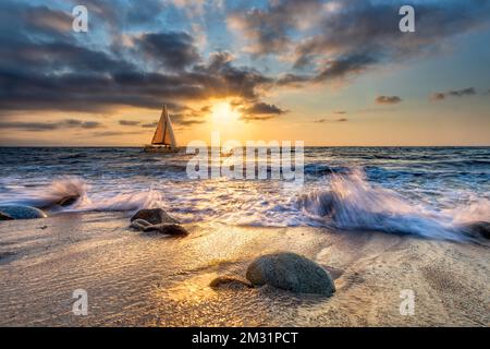 Ein Segelboot segelt entlang des Ozeans mit Wellenbrechern an der Küste Stockfoto