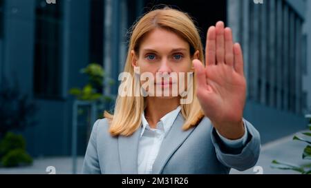 Eine ernsthafte Frau, die draußen steht und in die Kamera schaut, mit Stoppgesten, die Hand vor sich hält selbstbewusste Geschäftsfrau, die persönliche Grenzen schützt Stockfoto