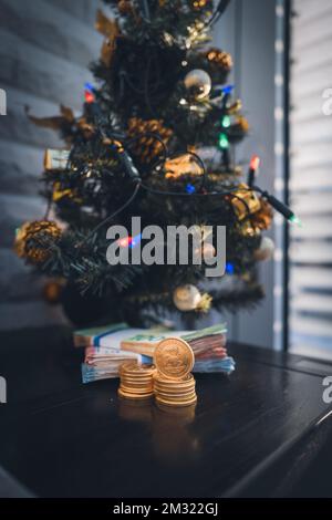 Unter einem weihnachtsbaum liegt ein Bündel Bargeld und ein Stapel Krugerrand-Goldmünzen Stockfoto