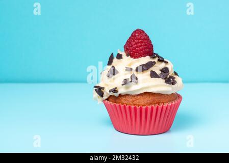 Cupcakes mit Schlagsahne dekorierten Schokoladenstreuseln und Himbeeren auf blauem Hintergrund Stockfoto