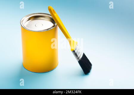 Gelbe Farbe in einem Glas mit einem Pinsel auf blauem Hintergrund. Hochwertiges Foto Stockfoto