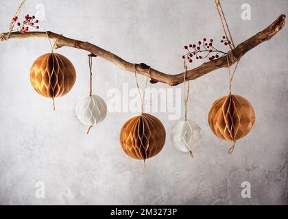 Handgefertigte Wabenkugeln aus Papier, die an einem Ast hängen. Schöne Weihnachtsdekoration für Zuhause. Skandinavisches Handwerkspapier Konzept. Stockfoto