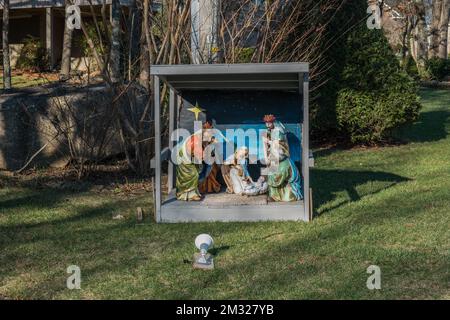 Alte Statuen von Maria, Joseph, Baby Jesus und dem drei Weisen in einem hölzernen Schutzhaus im Freien mit einer bemalten Szene im Hintergrund der Bethlehe Stockfoto