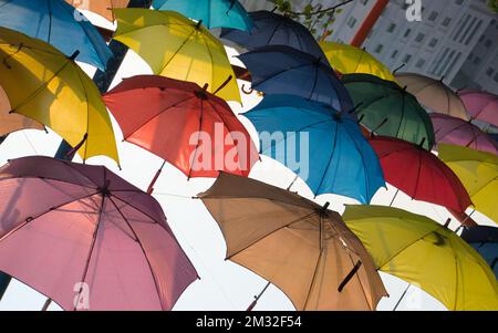 Mehrfarbige Regenbogenschirme, die auf dem Kopf hängen, als Straßenkunst. Farbenfrohe Ansicht. Stockfoto