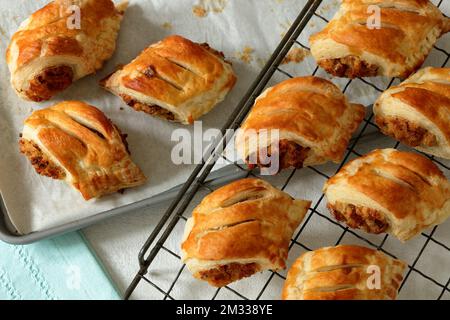 Frisch gebackene, hausgemachte vegetarische Wurstbrötchen mit Käselaibe, Zwiebeln und Brotkrumen, die auf einem alten Kühlregal aus Draht gekühlt werden Stockfoto