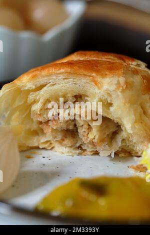 Nahaufnahme eines frisch gebackenen, hausgemachten, fleischfreien vegetarischen Wurstbrötchens mit Käselauch und Brotkrumen, serviert mit verschiedenen Gurken Stockfoto