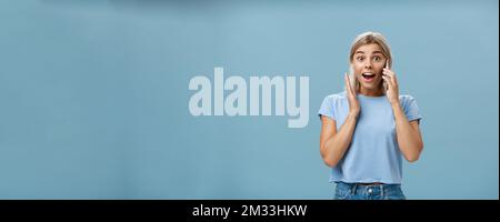 Freut mich, dass der beste Freund aus dem Ausland anruft. Porträt überrascht zufrieden charmante blonde Frau in trendigen T-Shirt Öffnung Mund aus Erstaunen Stockfoto