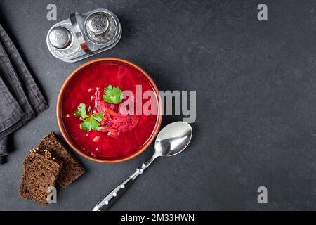 Traditionelle ukrainische Borschtsch-Suppe, vegetarische Gemüsesuppe aus roten Beeten in Schüssel auf schwarzem Betontisch. Draufsicht, Kopierbereich Stockfoto