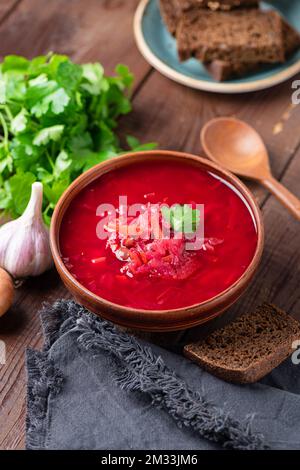 Vegetarischer Borscht serviert mit dunklem Roggenbrot in der Schüssel auf Holztisch. Ukrainische Küche. Rote-Bete-Gemüsesuppe Stockfoto