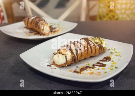 italienischer Cannoli-Kuchen mit Pistazien und Schokolade, zwei Stücke auf verschiedenen Tellern Stockfoto