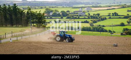 County Cork, Irland, 20. August 2022. Ein blauer Traktor sät an einem Sommertag in Irland ein gepflügtes Feld. Landwirtschaftliche Arbeit auf einem irischen Hof, landwirtschaftlich Stockfoto