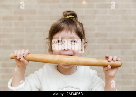 Das süße Mädchen bereitet sich in der Küche vor. Das lustige kleine Mädchen hat Spaß mit dem Spieß für Teig. Stockfoto