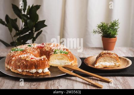 Roscon de reyes mit einem Stück, das auf einer Holzplatte geschnitten wurde und die Creme der Füllung enthüllt. Nahaufnahme. Stockfoto