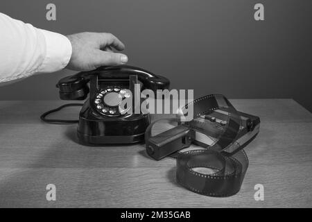 Alte Filmkamera, Film, altes Handy. Männliche Hand nimmt das Telefon. Retro-Szene. Schwarzweißfoto Stockfoto