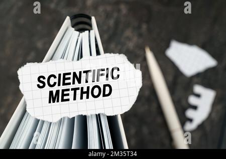Auf dem Tisch befindet sich ein Notizbuch, auf dem ein Stück zerrissenes Papier mit der Aufschrift „Scientific Method“ (Wissenschaftliche Methode) liegt. Der Stift liegt außerhalb der Schärfezone. Stockfoto