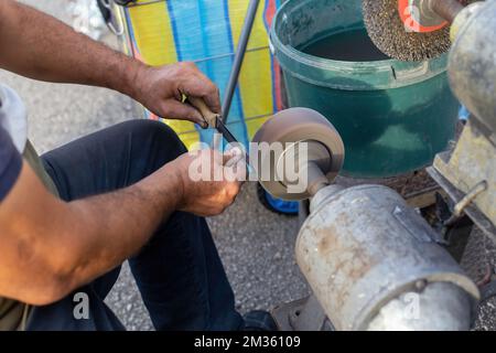 Ein Mann, der auf dem Markt ein Messer schärft. Metallmesser Stockfoto