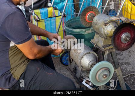 Ein Mann, der auf dem Markt ein Messer schärft. Metallmesser Stockfoto