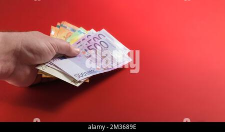 Bargeld in der Hand eines Mannes auf einem roten Tischhintergrund. Handgehaltenes Banner für Euro-Banknoten Stockfoto