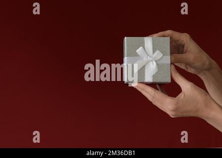 Zeit für Geschenke Eine Frauenhand hält eine Geschenkbox auf rotem Burgund. Minimalismus. Speicherplatz kopieren Stockfoto