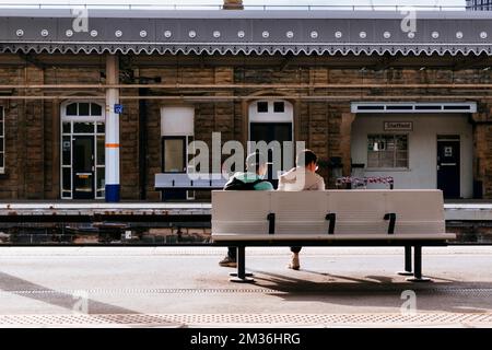 Zwei Leute sitzen auf einer Bank und warten auf den Zug. Bahnhof Sheffield. Sheffield, South Yorkshire, Yorkshire und The Humber, England, United Ki Stockfoto