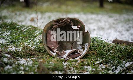 Ein russischer Militärhelm aus der Zeit des Zweiten Weltkriegs auf dem schneebedeckten Gras in einem frei besetzten Dorf in der Oblast Kherson, Ukraine Stockfoto