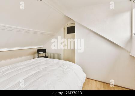 Ein Bett in einem Zimmer mit weißen Wänden und Holzfußboden an der Seite des Bettes ist eine elektrische Heizung Stockfoto