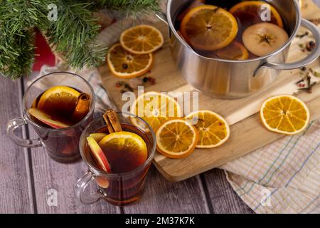 Glühwein in Glasbecher gegossen, Pfanne mit heißem Weihnachtspunsch auf Holztisch, Rotwein Stockfoto