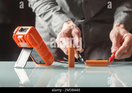 Elektriker, der die Batteriespannung mit einem Multimeter misst. Home Master und tragbarer Energieeffizienzbereich Stockfoto