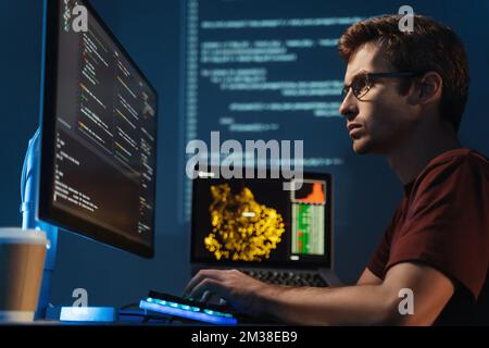 Seitenansicht eines intelligenten Programmierers, der auf einen großen Monitor schaut, die id-Adresse und das Debugging-System überprüft, HTML-Code schreibt, bis spät in der Nacht am Tisch sitzt und einen gezoomten digitalen Hintergrund betrachtet Stockfoto