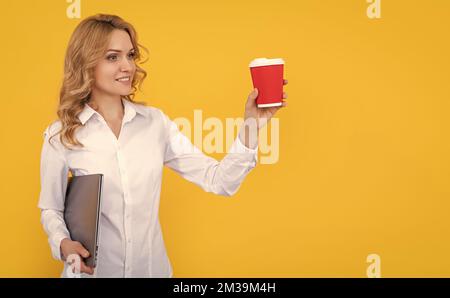 Glückliche blonde Frau mit Kaffeetasse und Computer auf gelbem Hintergrund Stockfoto