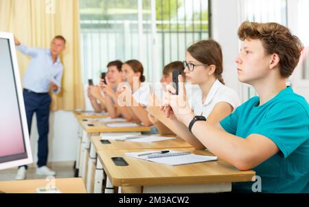 Klassenkameraden nutzen ihre Smartphones während der Nahaufnahme des Unterrichts stark Stockfoto