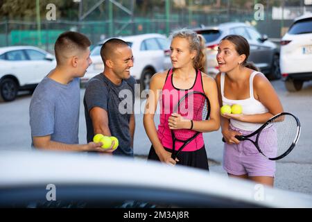 Zwei Tennisspielerpaare diskutieren gerne das letzte Spiel auf dem Parkplatz Stockfoto