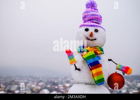 Frohe Weihnachten und Frohes neues Jahr. Lächelnder Schneemann mit Hut, Schal und Fäustlingen mit Weihnachtsspielzeug. Stockfoto